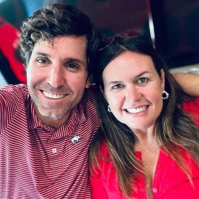 Bryan Sanders is wearing a red polo shirt. His wife is also wearing a red dress